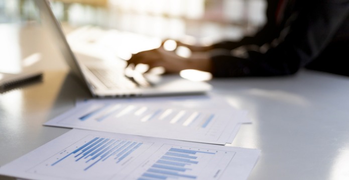 Blurry figure working at laptop with financial charts in the foreground