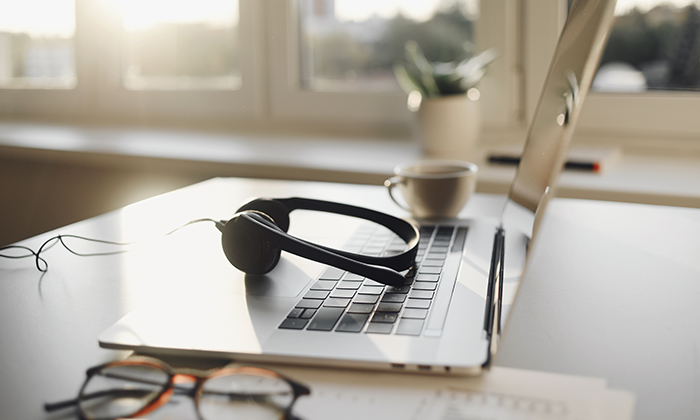 Black headphones on a laptop with a coffee cup and glasses on a sunlit desk.